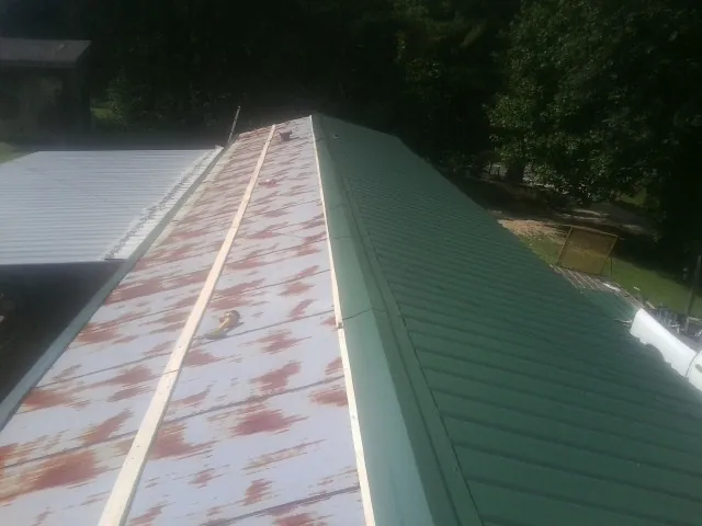 Old rusted panels beside newly installed green metal roofing — Wind Damage Roof Repair by Roofing Brothers in Saint James