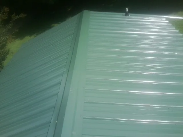 New green metal panels meeting at the ridge of a roof — Flat Roof Repair work by our crew in Saint James