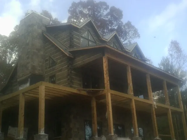 Stone chimney and dormers on a large log home with a timber porch in Saint James