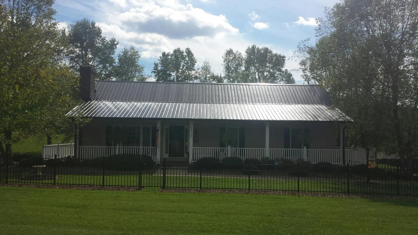 Gray metal roof on a brick ranch with a full width front porch — Gutter Guard Installation work by our crew in Saint James