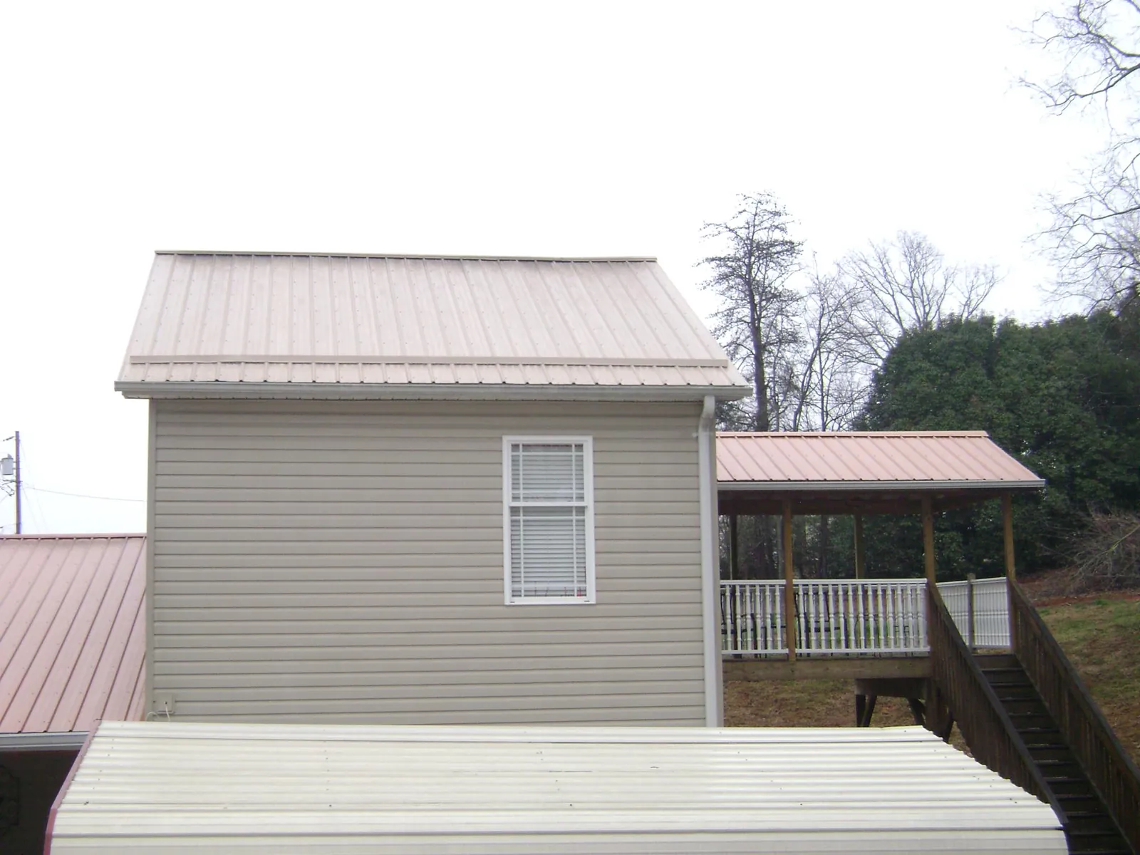 Tan metal roofs on a two story addition and attached porch, from a Roof Replacement job in Saint James